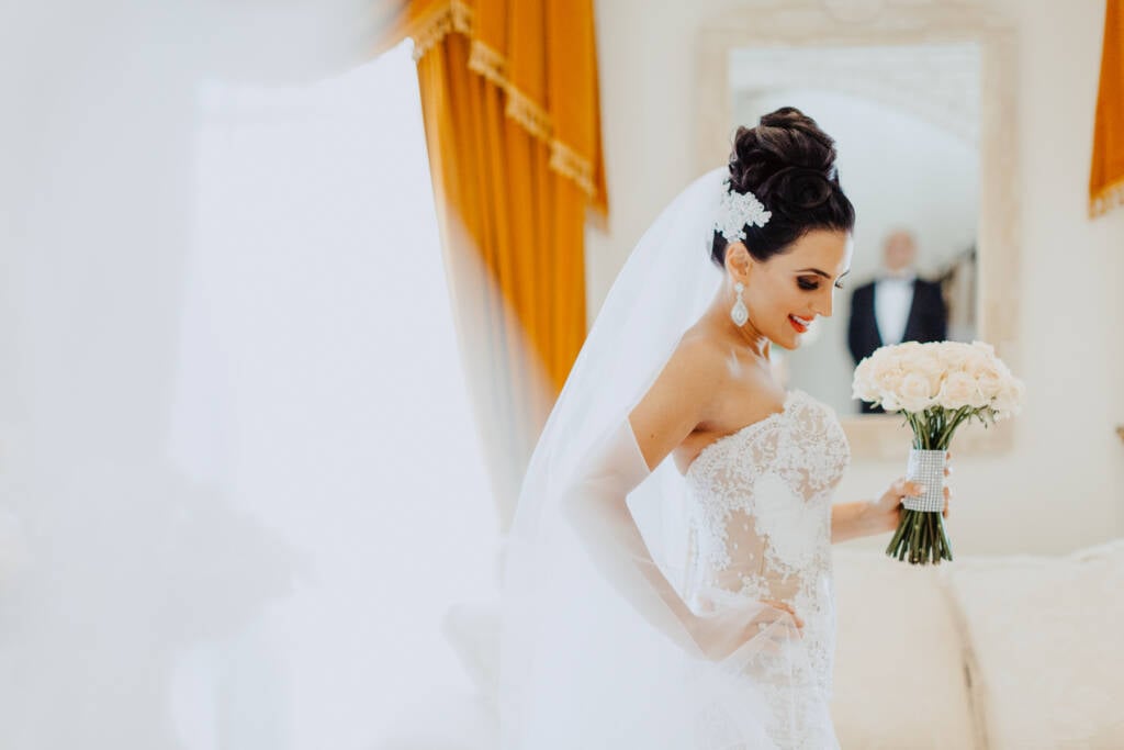 Danielle looks down at her bouquet with her veil spread around her