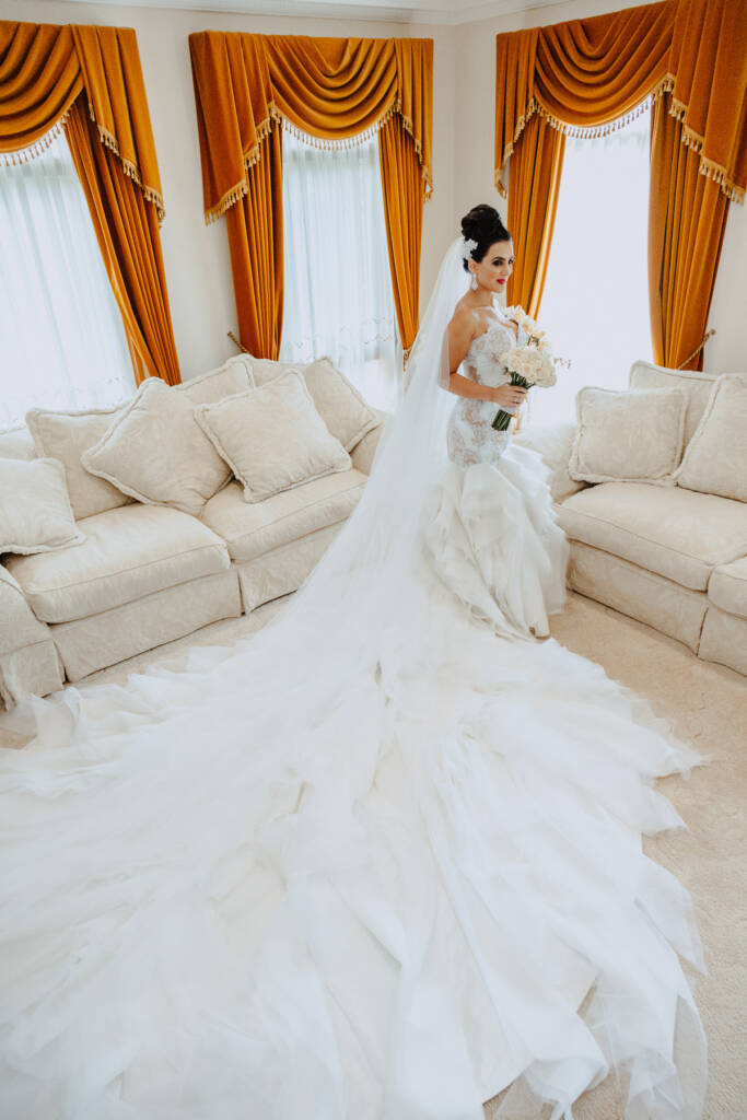 Danielle stands between cream sofas with her gown's train spread around her