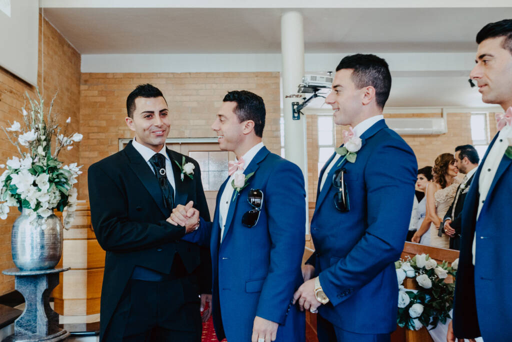 Michael clasps a groomsman's hand at the front of St Aphrem