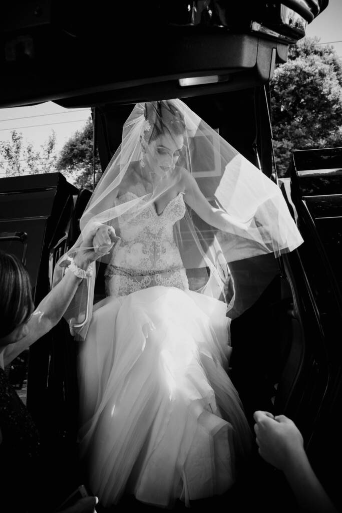 Black-and-white photo of Danielle stepping from the wedding car with her veil over her face