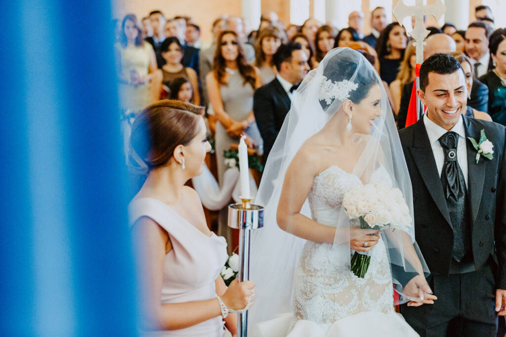 Danielle and Michael hold hands beside a lit ceremony candle at St Aphrem Syrian Orthodox Church