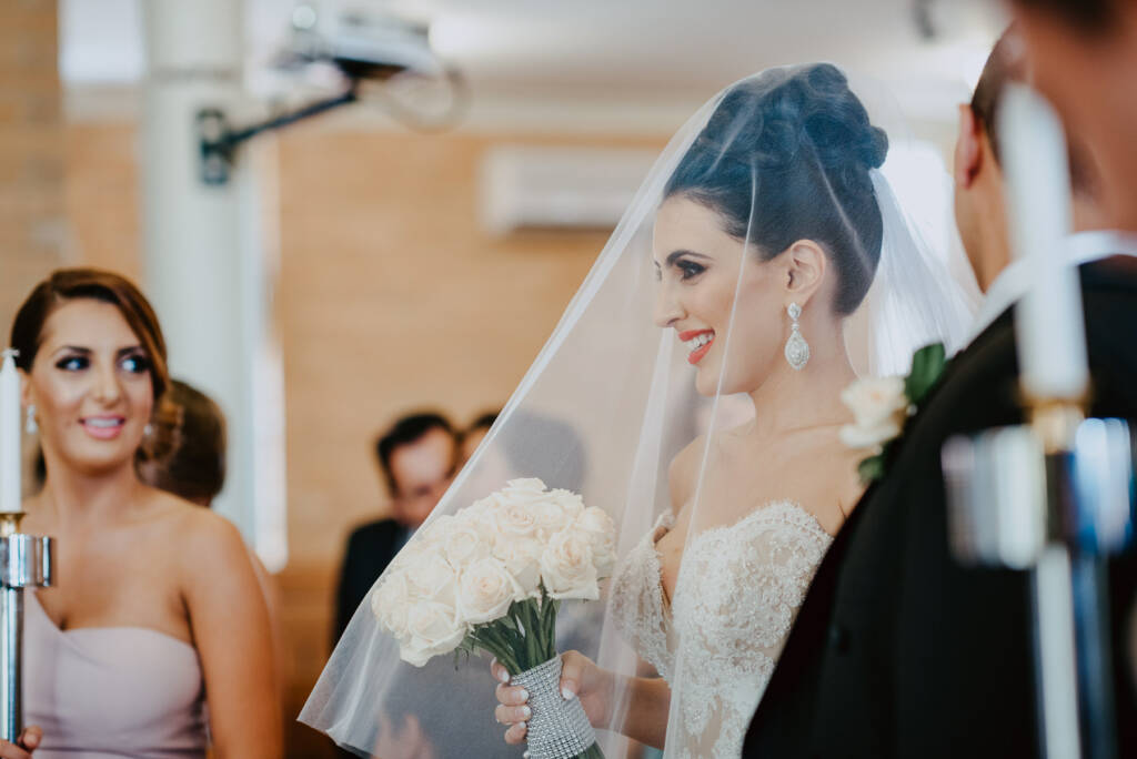Danielle smiles beneath her veil while holding her bouquet during the ceremony