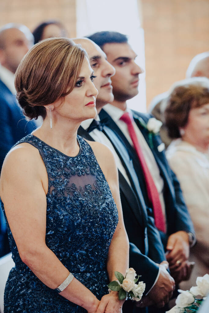 A guest in a navy dress watches the ceremony from a pew at St Aphrem