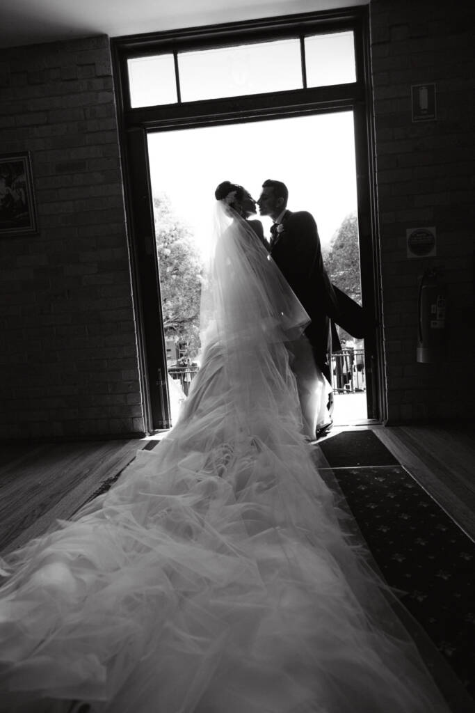 Danielle and Michael lean towards each other in the bright doorway of St Aphrem