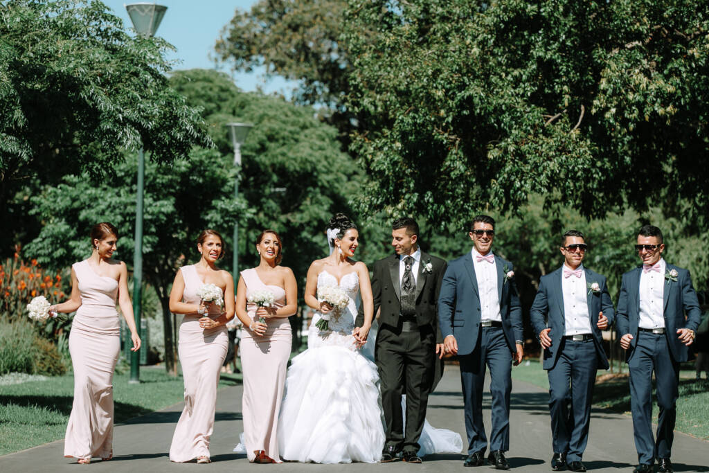 The wedding party walks along a tree-lined path at Carlton Gardens in Melbourne