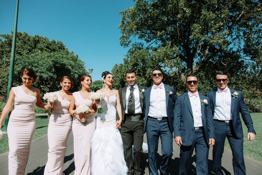 Danielle, Michael and their attendants walk arm in arm along a Carlton Gardens path