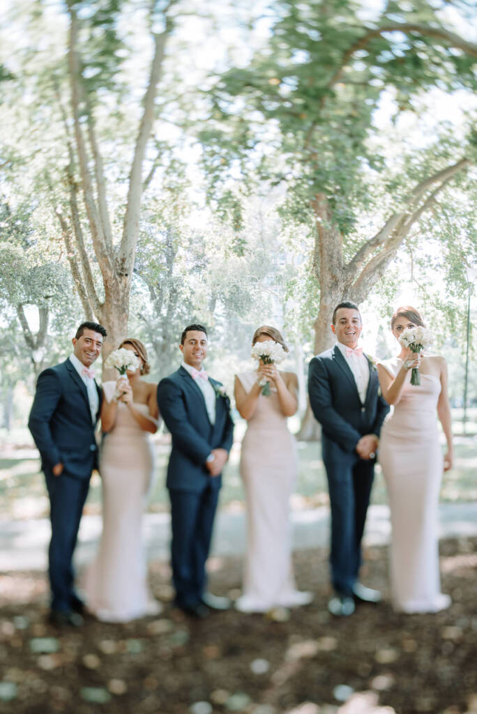Bridesmaids raise bouquets towards their faces beside the groomsmen at Carlton Gardens