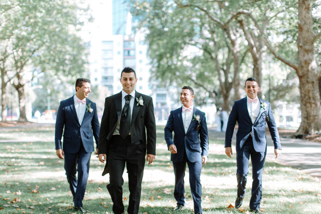 Michael and his groomsmen walk across the lawn at Carlton Gardens in Melbourne