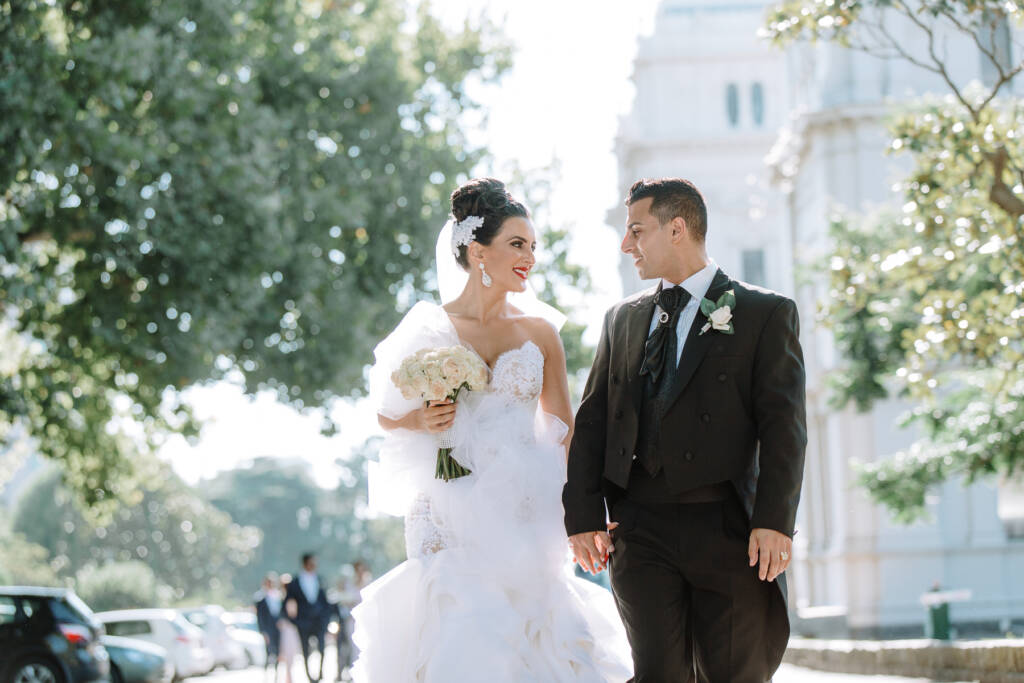 Danielle and Michael hold hands in front of the Royal Exhibition Building at Carlton Gardens
