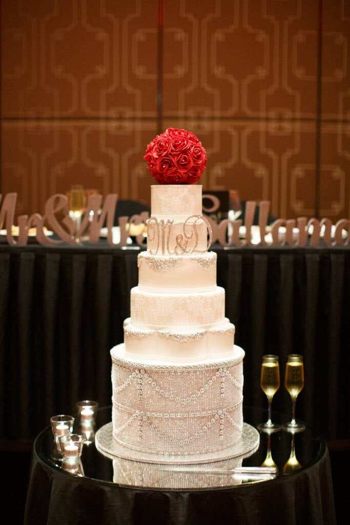 A tall wedding cake with red roses stands in the Palladium at Crown ballroom