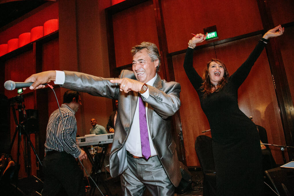 A performer holds a microphone towards guests while a woman raises her arms at Palladium