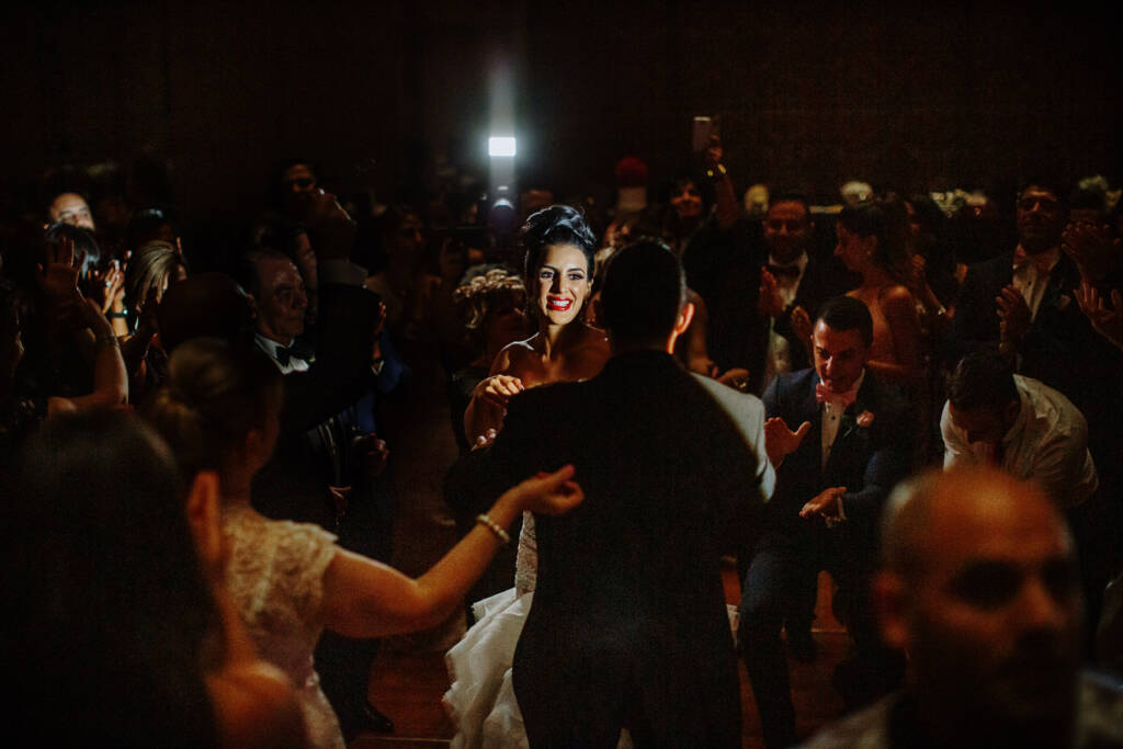Danielle smiles towards Michael among clapping guests in the dimly lit Crown Palladium ballroom