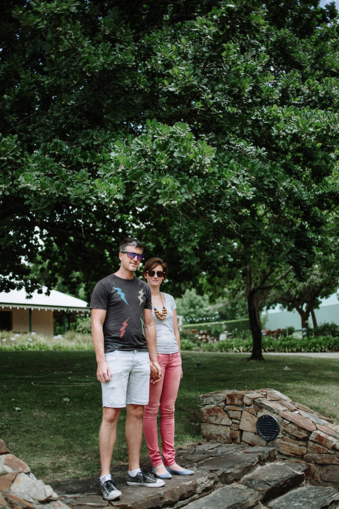 Camilla and Jason hold hands on stone steps beneath a tree during their Flowerdale Estate engagement shoot.