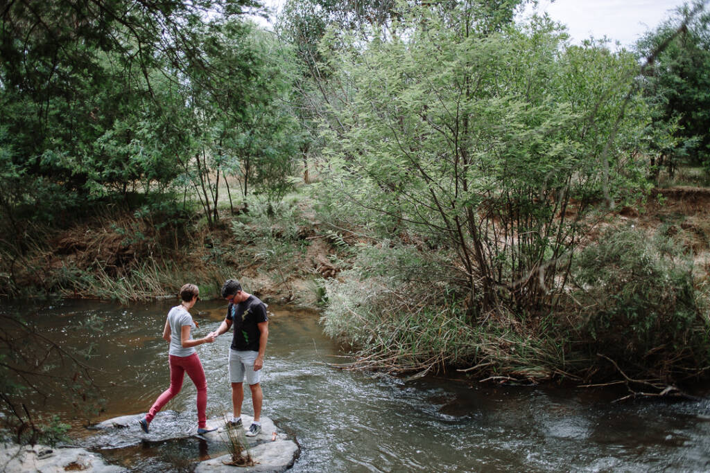 Camilla and Jason step between rocks in a shallow stream at Flowerdale during their engagement shoot.