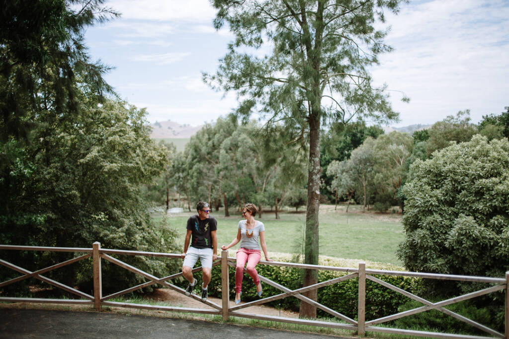 Wide engagement portrait of Camilla and Jason on a fence above the lawns at Flowerdale Estate.