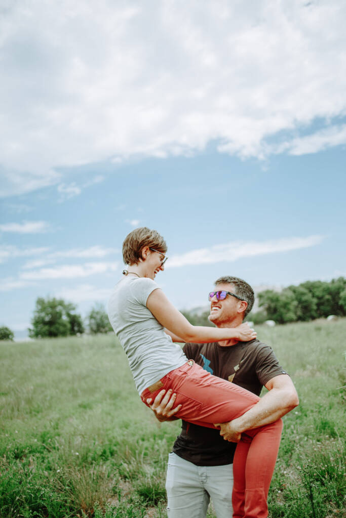Jason lifts Camilla in a grassy field at Flowerdale Estate during their engagement shoot.