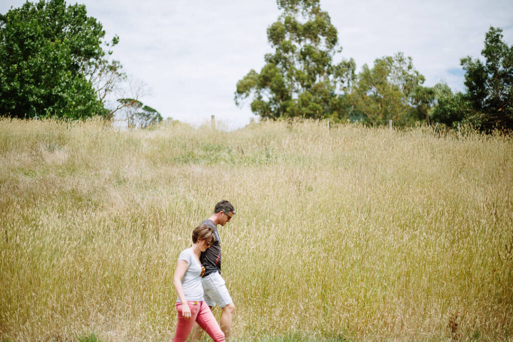 Camilla and Jason walk through long grass at Flowerdale in casual clothes.