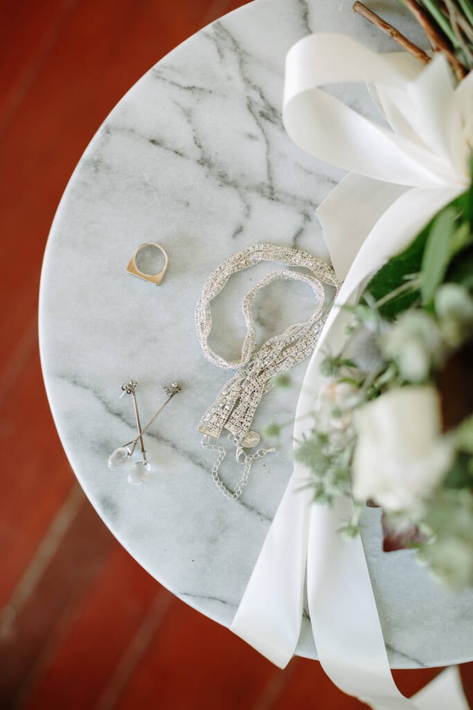 Earrings, a ring and bridal jewellery arranged beside bouquet ribbon for Camilla's wedding.