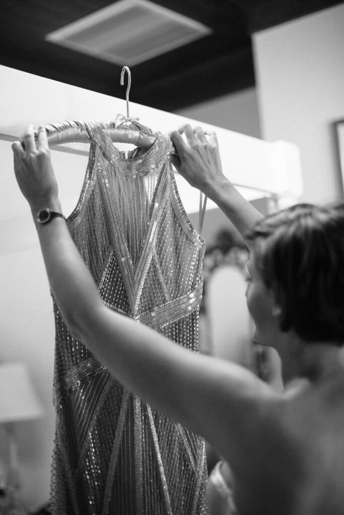 Black and white photo of Camilla lifting her heavily beaded geometric gown on a padded hanger.