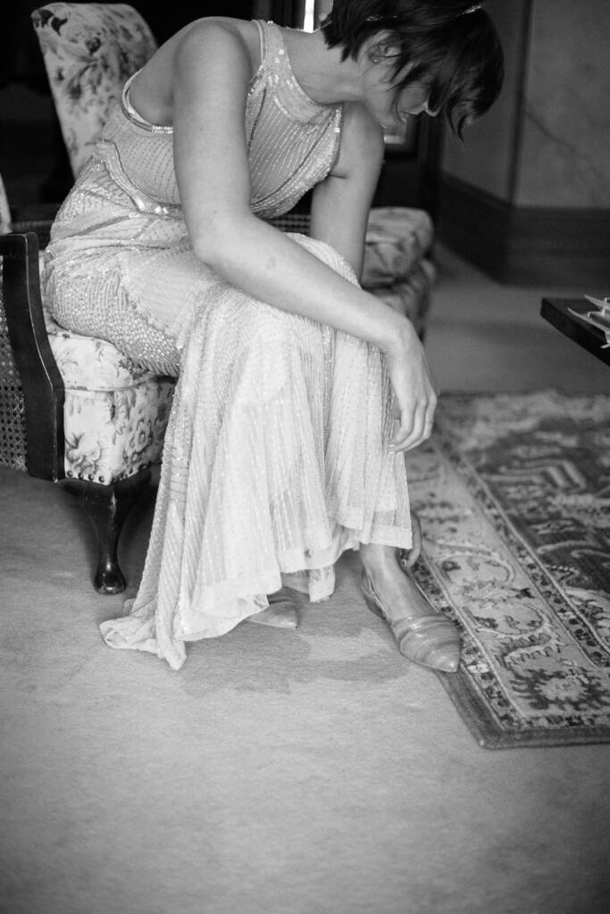 Camilla bends towards her shoe while seated in a furnished room at Flowerdale.