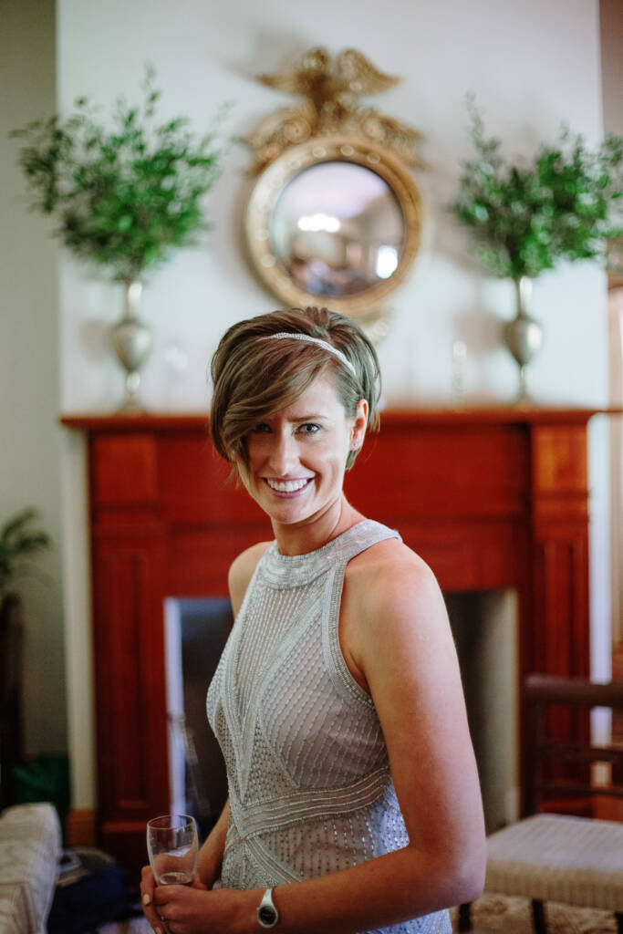 Camilla smiles with a glass before the fireplace and mirror inside Flowerdale Estate.