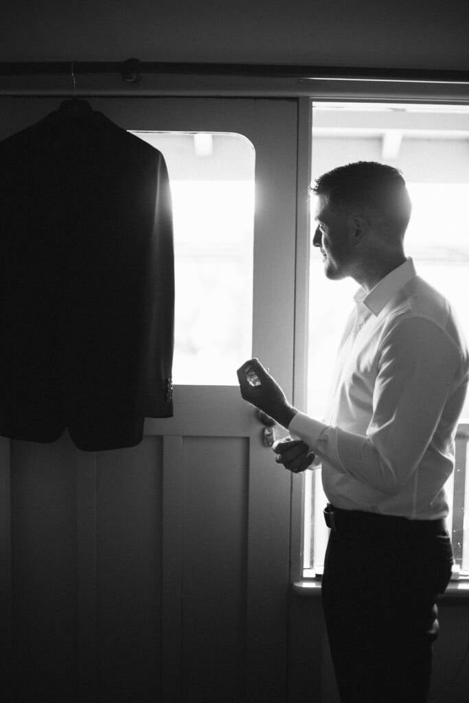 Black-and-white portrait of Jason adjusting his cuff beside a glazed door at Flowerdale.