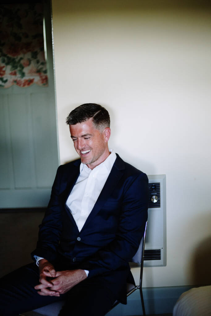 Jason smiles while seated in his navy suit on the wedding morning.