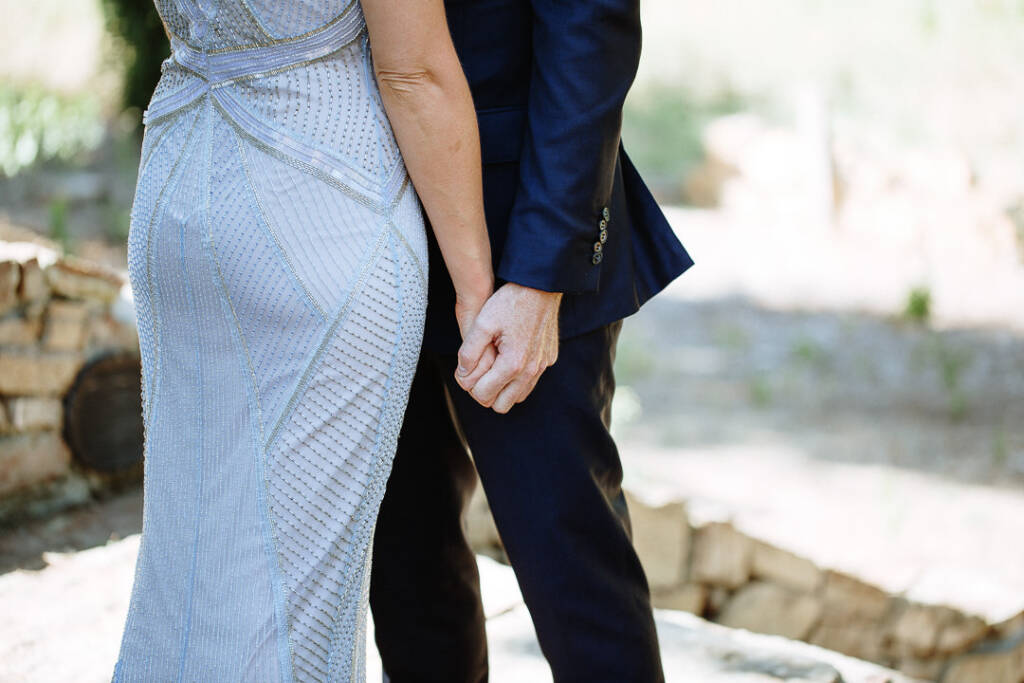Close detail of Camilla and Jason holding hands beside her beaded gown.