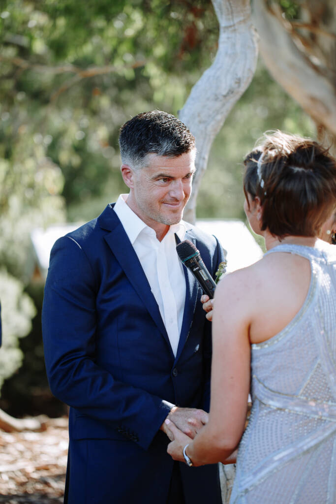 Camilla and Jason hold hands as a microphone is held near them during the ceremony at Flowerdale.