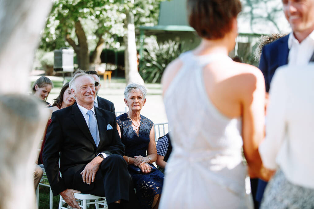 Past Camilla's shoulder, guests smile from white ceremony chairs at Flowerdale Estate.