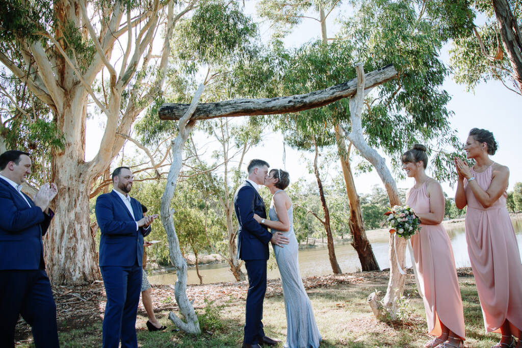Camilla and Jason kiss beneath the timber arbour beside the lake at Flowerdale.