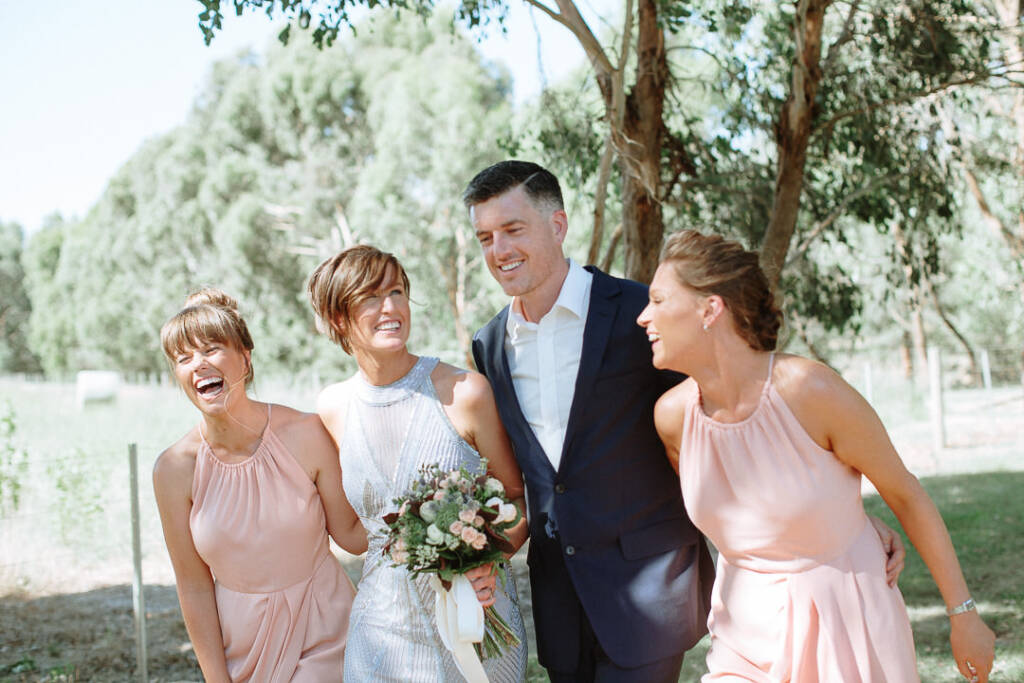 Camilla and Jason laugh in a group portrait with two pink-dressed attendants.