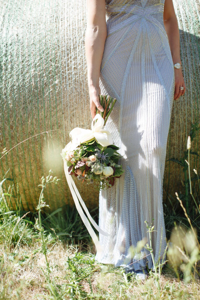 Camilla's ribboned bouquet hangs beside her beaded gown and a hay bale at Flowerdale.