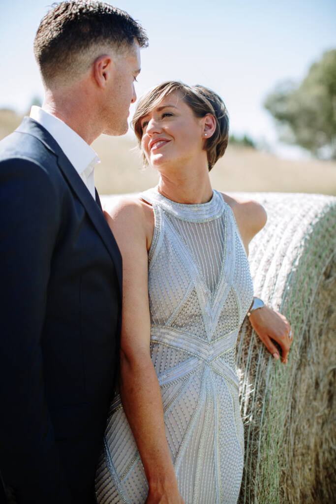 Camilla smiles up at Jason beside a round hay bale at Flowerdale Estate.