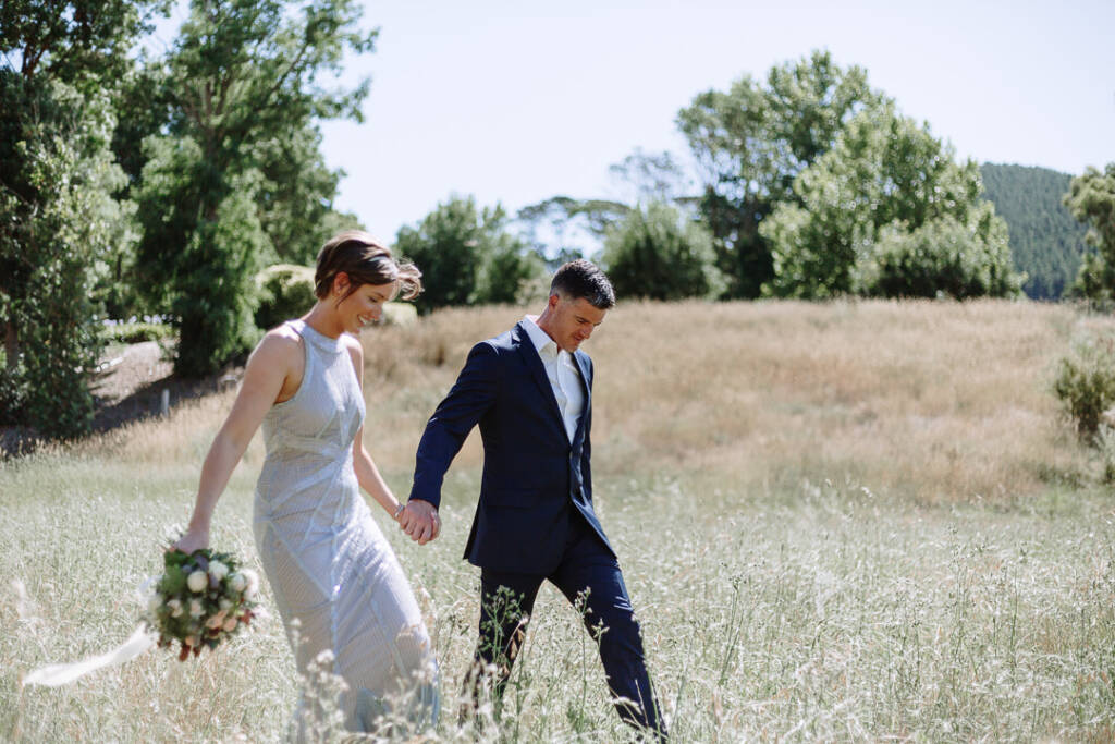 Camilla and Jason walk hand in hand through long grass at Flowerdale Estate.