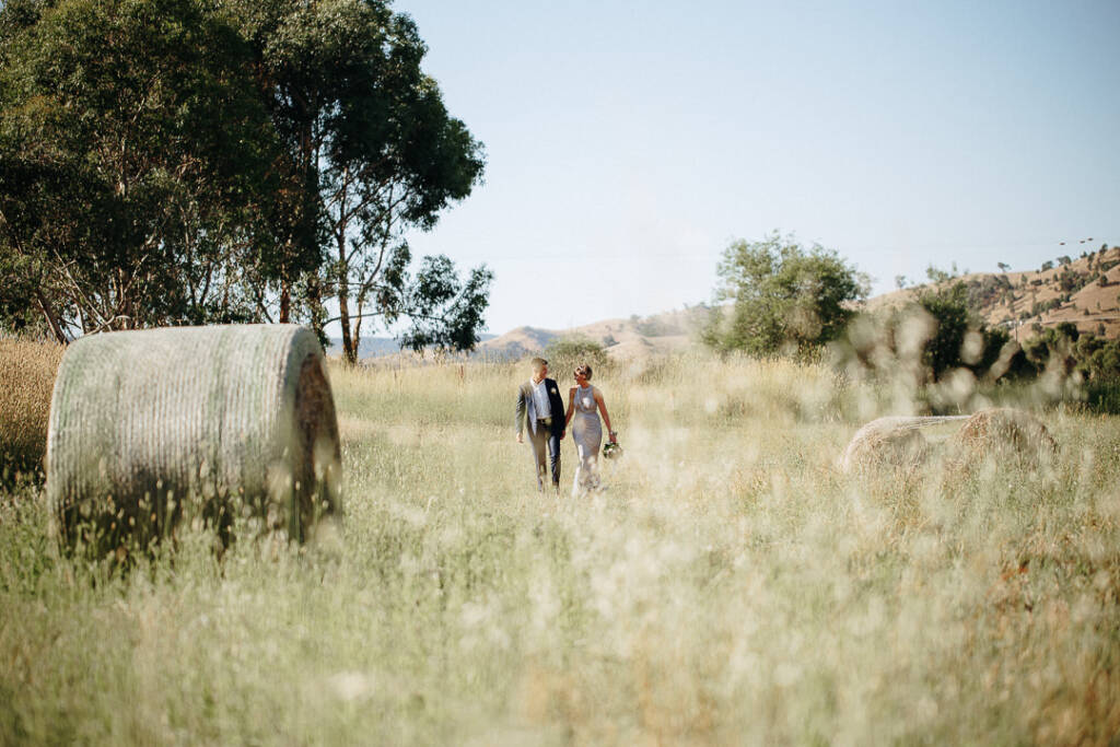 Camilla and Jason walk between round hay bales at Flowerdale Estate.