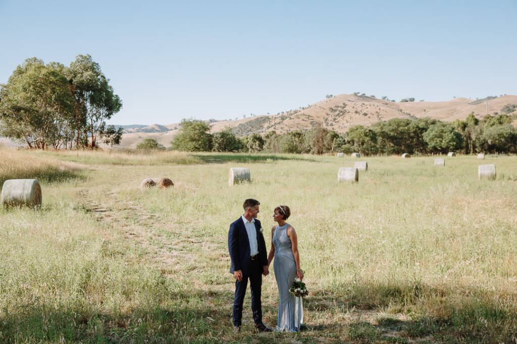 Wide portrait of Camilla and Jason beside hay bales and hills at Flowerdale.