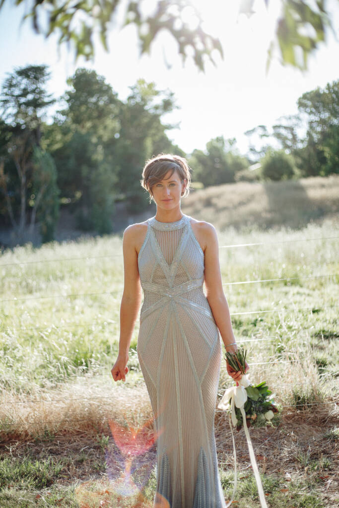 Backlit bridal portrait of Camilla with a bouquet and lens flare by a Flowerdale paddock fence.