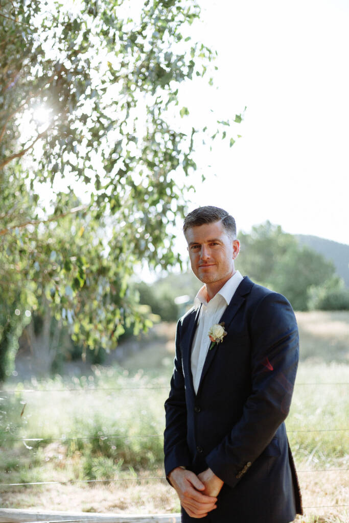 Jason stands with hands clasped beneath leafy branches at Flowerdale Estate.