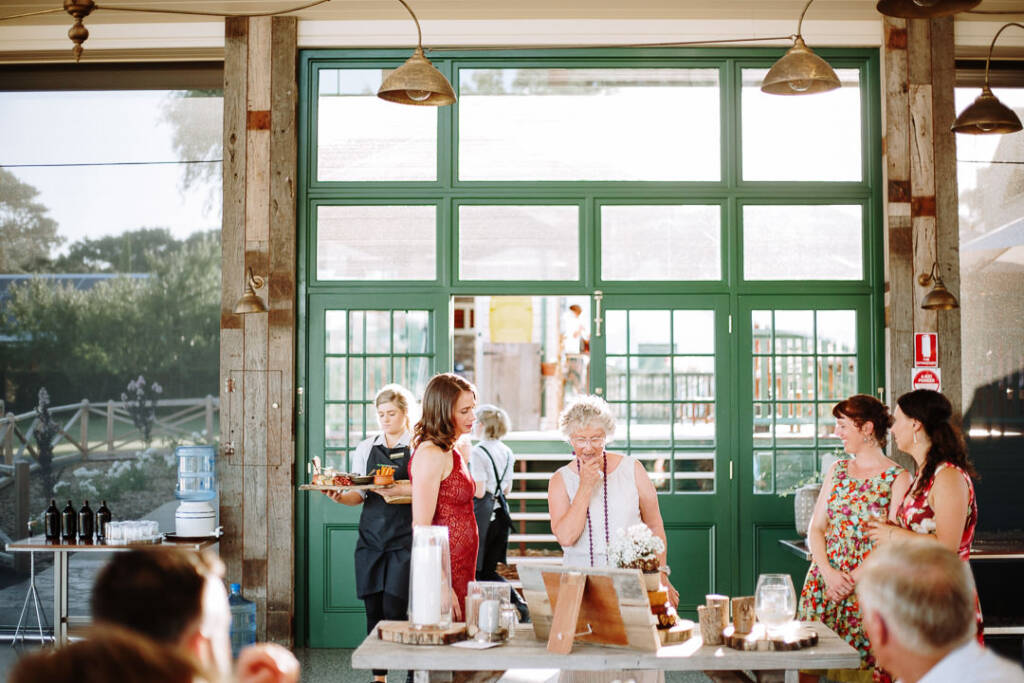An apron-wearing server carries a tray beside guests inside Flowerdale Estate's reception pavilion.
