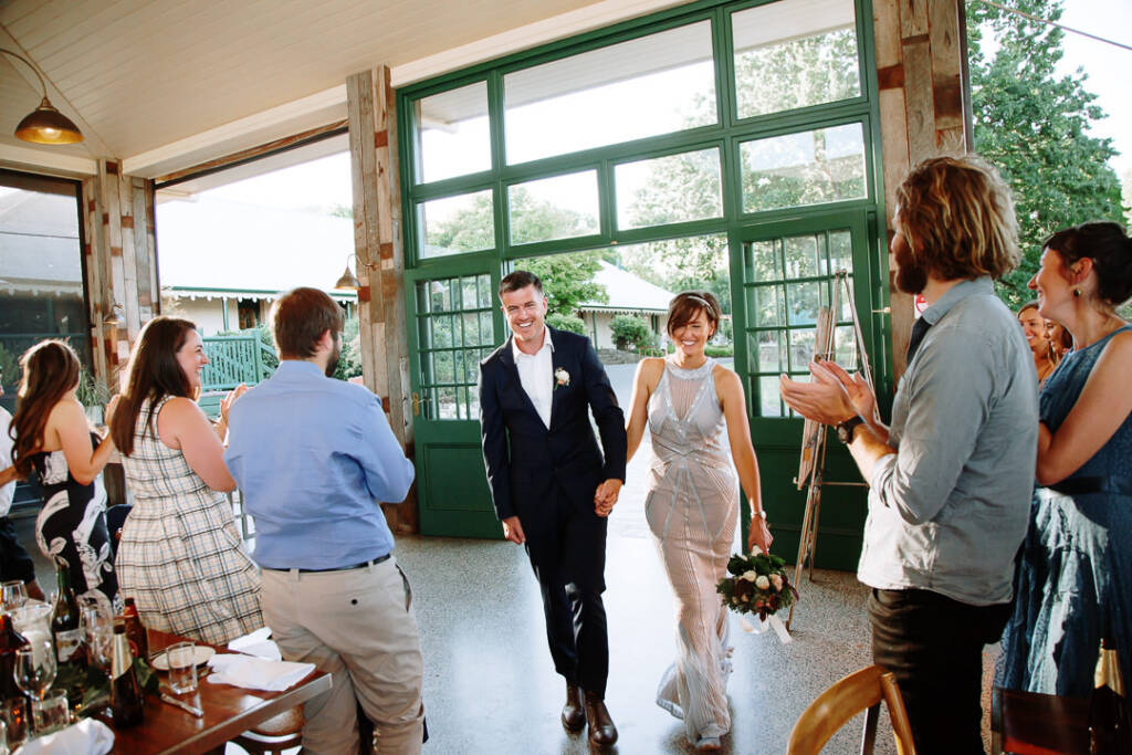 Camilla and Jason enter the Flowerdale Estate pavilion through green doors as guests applaud.
