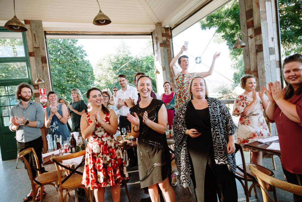 Guests stand and applaud beneath the pendant lights in Flowerdale's reception pavilion.