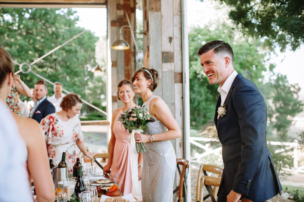 Camilla and Jason stand smiling beside a set table in the Flowerdale Estate pavilion.