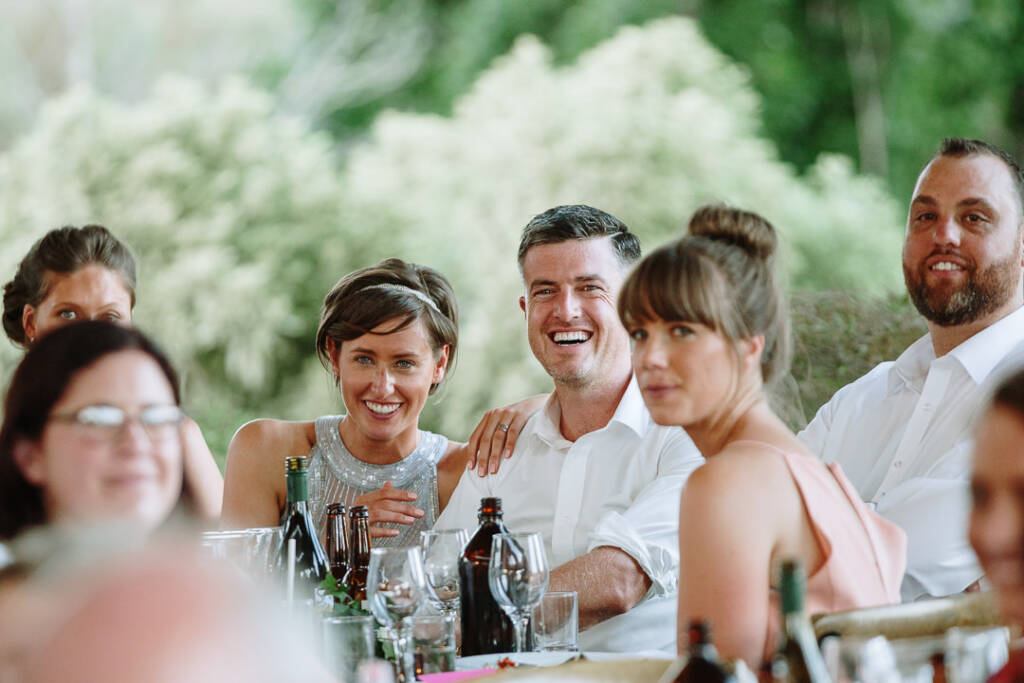 Camilla and Jason smile while seated with attendants at the Flowerdale reception table.