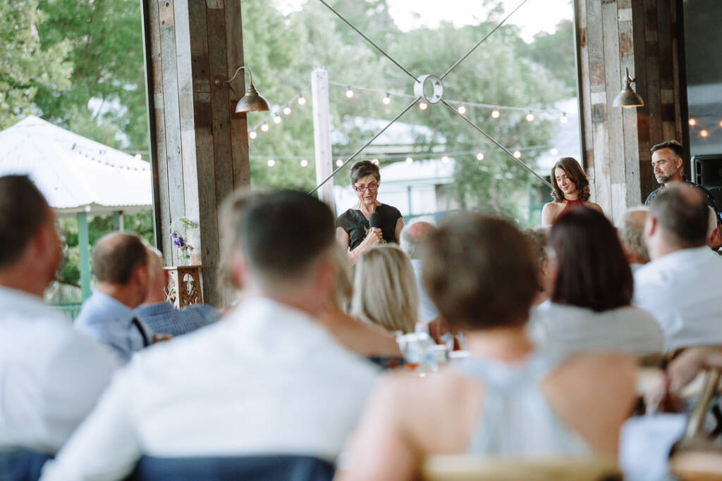 A guest holds a microphone before seated guests in the Flowerdale Estate pavilion.