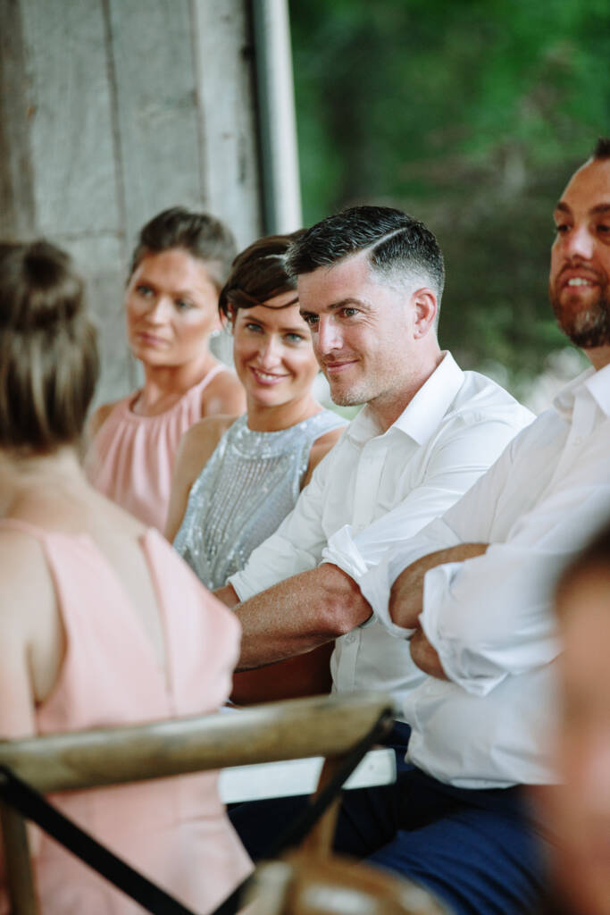 Camilla and Jason smile while seated with attendants at their wedding reception.