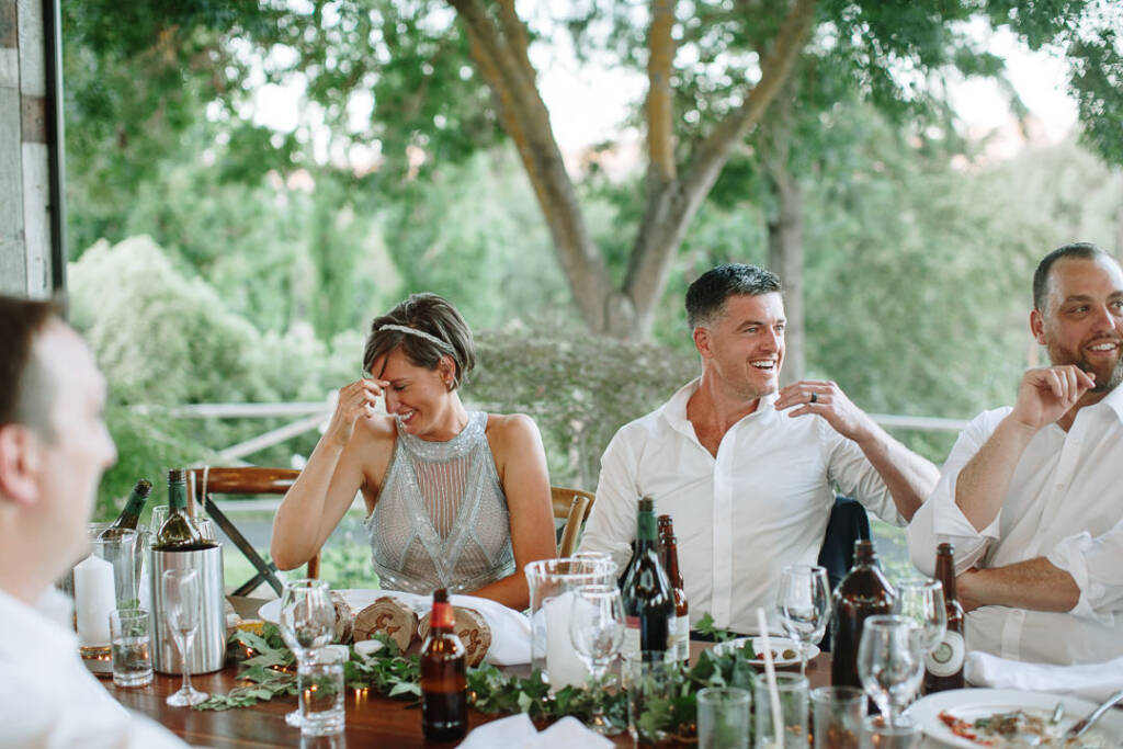 Camilla holds a tissue near her eye while Jason laughs at their Flowerdale reception table.