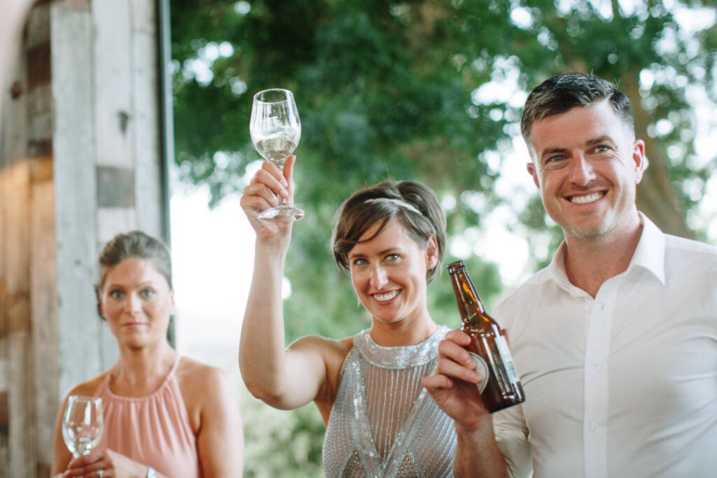 Camilla raises a wine glass high and Jason lifts a beer as they toast.