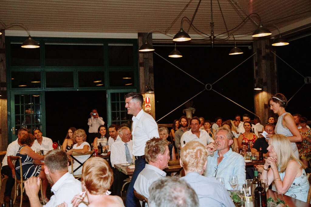 Camilla and Jason stand among seated guests beneath the Flowerdale pavilion lights.