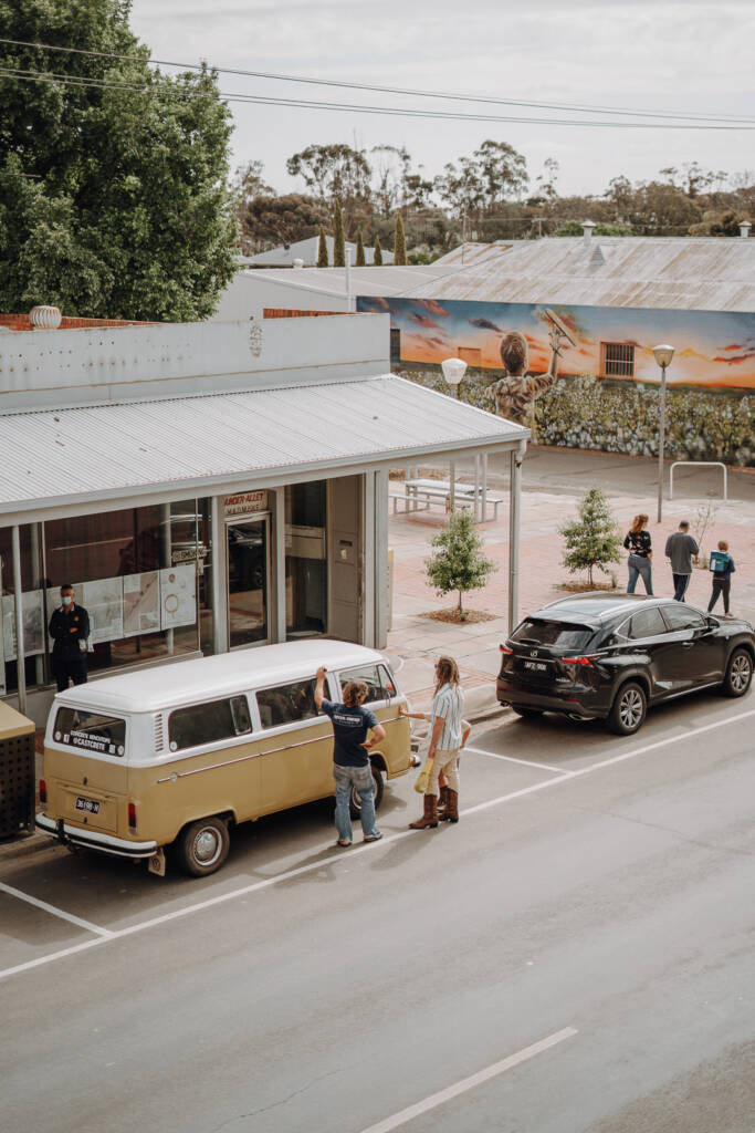 A yellow-and-white van stands across the street from a painted mural, viewed from Royal Hotel Sea Lake.